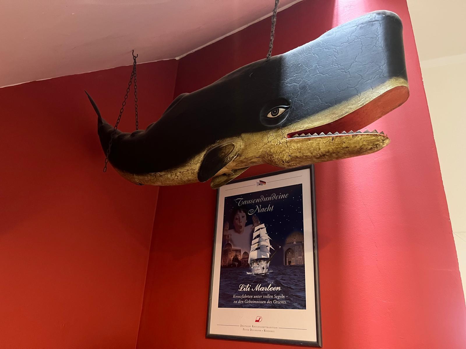 Geschnitzter Wal über einem Lili-Marleen-Poster im roten Flur