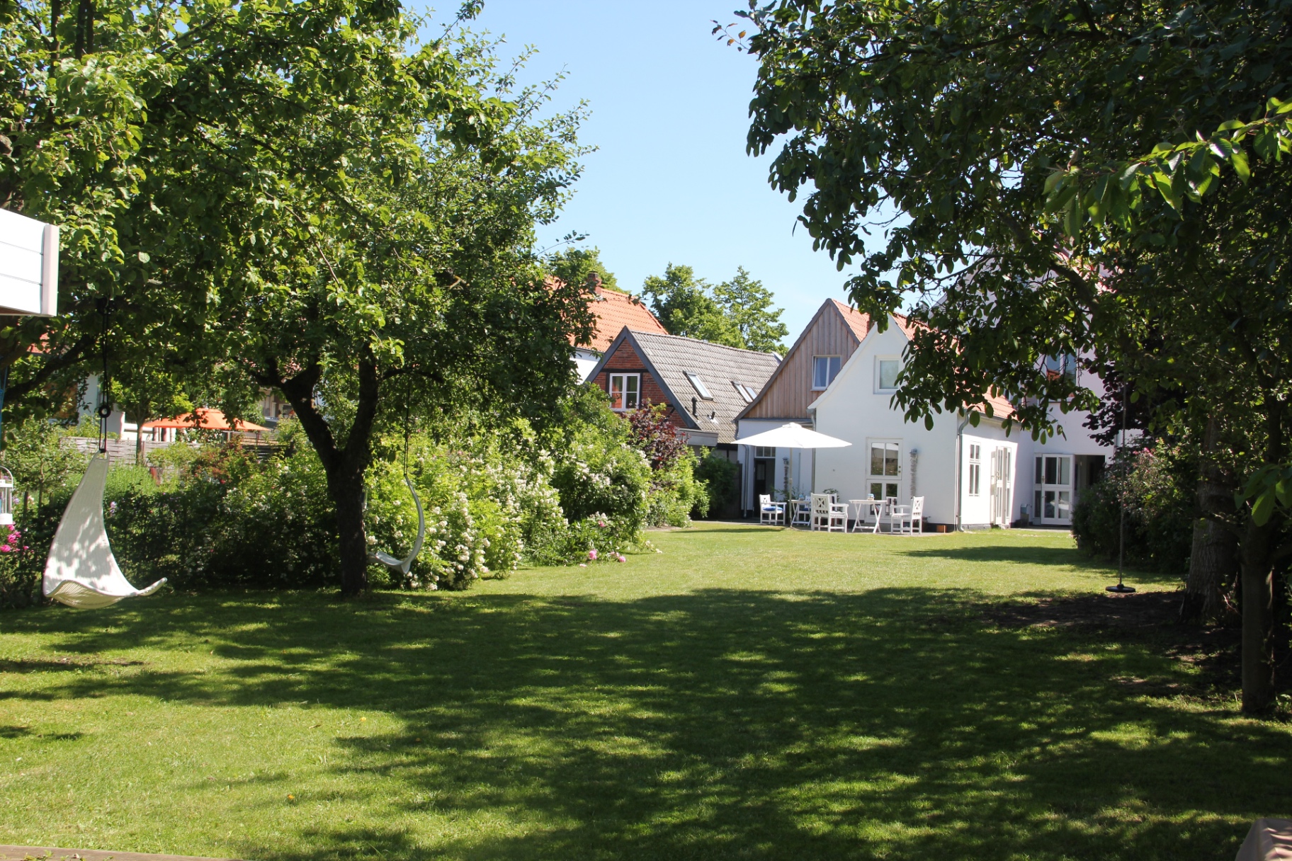 Sonniger Hotelgarten mit Hängesessel und Blick auf das Haus